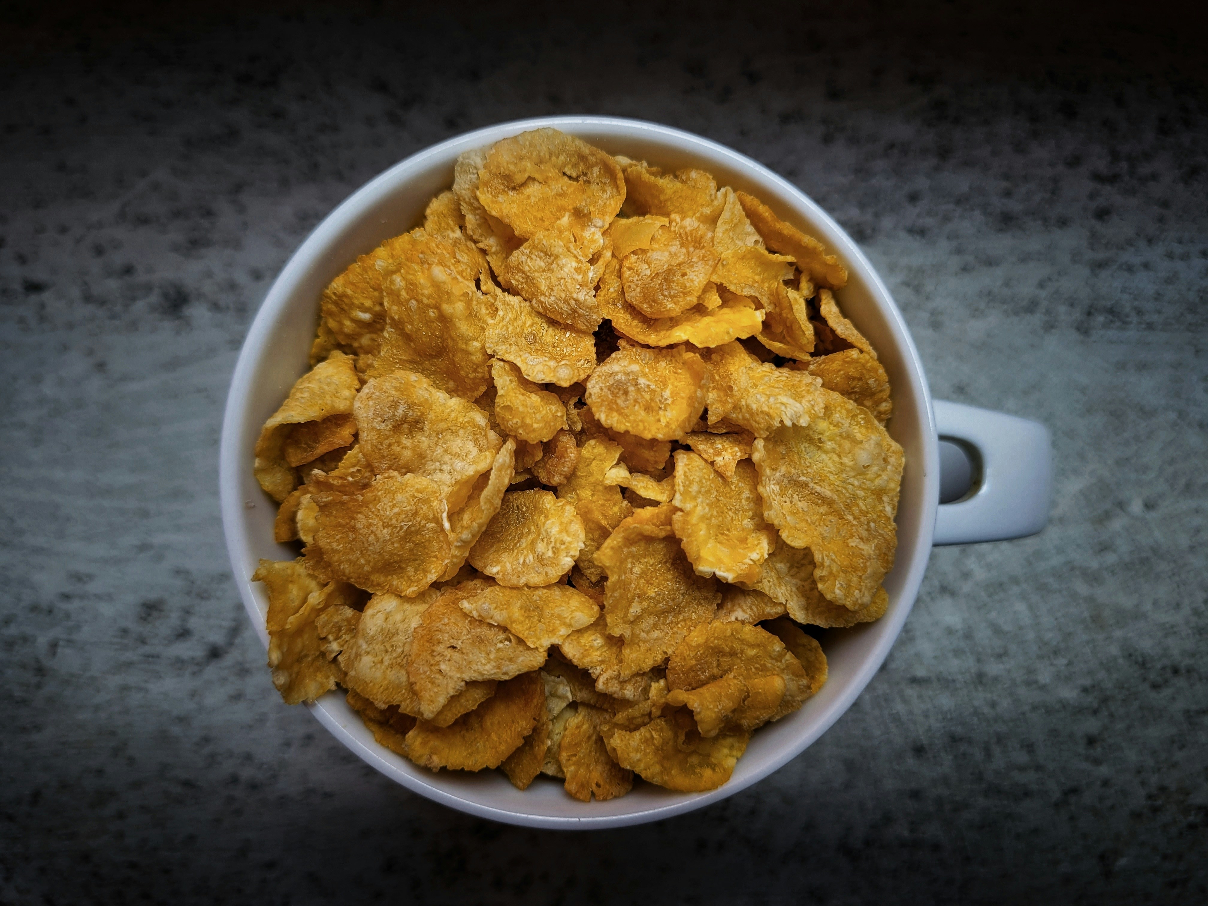 Cornflakes in a white mug photographed from above on a grey stone surface
